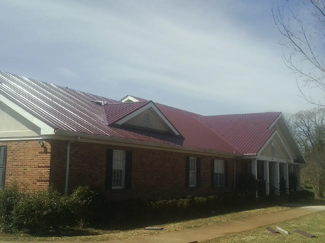 Red metal roof with gabled entries on a long brick building, from a Hail Damage Roof Repair job in The Dalles