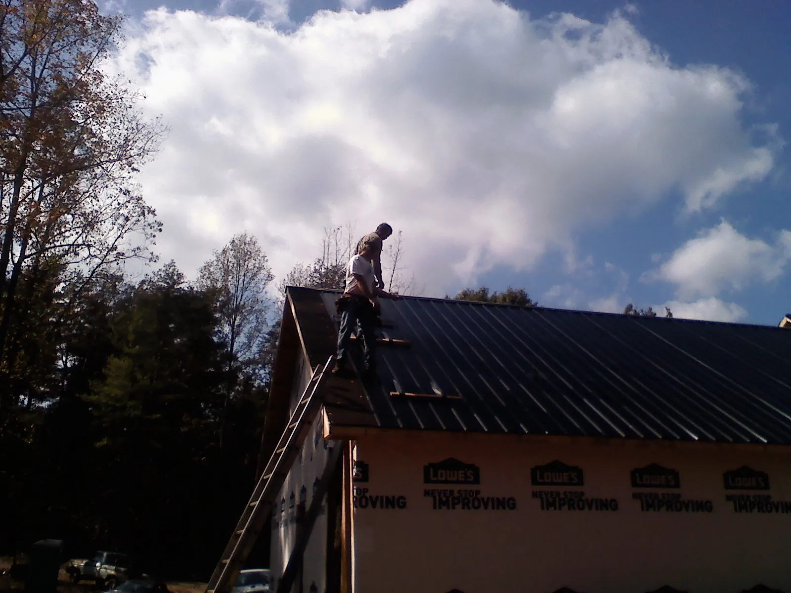 Roofer fastening dark metal panels high against a cloudy sky, from a Roof Inspection job in The Dalles