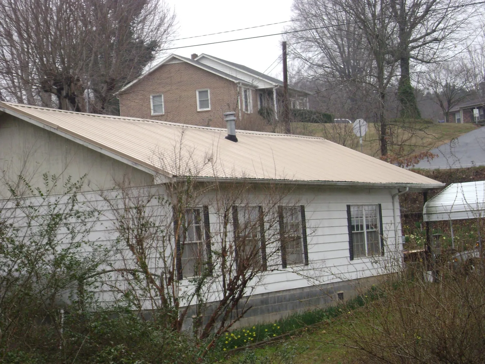 Tan metal roof on a white sided house set into a hillside — Commercial Roofing by Roofing Brothers in The Dalles